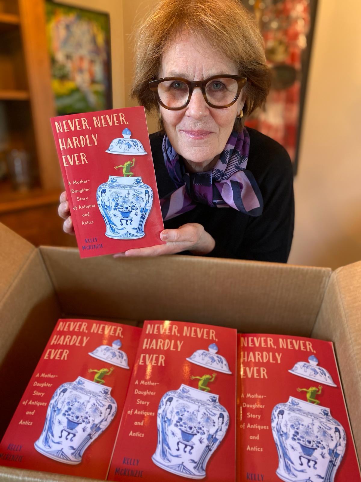 woman holding up her debut book overtop box of others